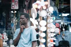 Man in a light blue shirt stands thoughtfully near a display of various illuminated lights in a shop.
